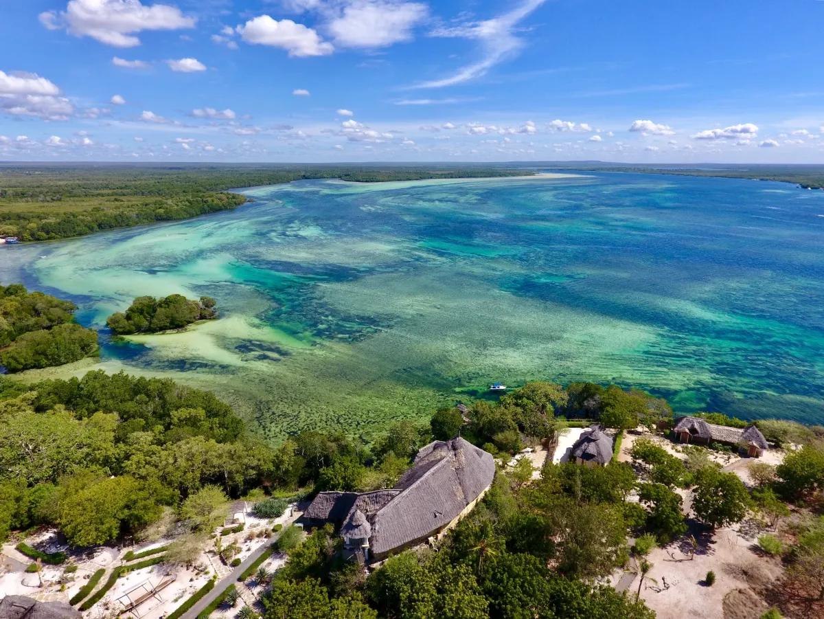 Aerial panorama of the Mida Creek lagoon and mangrove forest with the resort’s thatched roofs on the shoreline below
